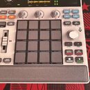 Bílo sampler MPC SAMPLE značky AKAI professional. Zařízení má displej s vizualizací zvukové vlny, několik ovládacích knoflíků a mřížku šestiдесяti čt…