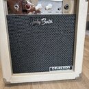 Kytarový kombozesilovač v bílém vinylovém potahu s kovovými rohy. Na předním černém textilním krytu je nápis „Harley Benton“ a v pravém dolním rohu š…