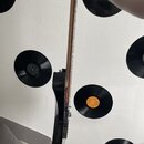 Fotografie zachycuje detail krku a části korpusu černé elektrické kytary. Hmatník je vyroben z tmavého dřeva s viditelnými pražci a bílými tečkovými…