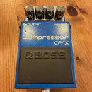 Modrý efekt pedál s černým gumovým plátkem. Na horní části je nápis Compressor CP-1X a logo BOSS. Pedál má čtyři kovové ovládací knoflíky a nápisy OU…