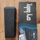Černý wah pedál s žebrovaným povrchem šlapací plochy a přiloženou originální krabicí. Na pedálu jsou vlevo nápis AMP INPUT a vpravo INSTRUMENT. Na kr…