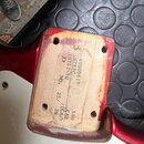 Detail zadní části červené elektrické kytary s viditelným dřevěným blokem pod mostem. Na dřevě je vyryto: 40000517, ST57C, ST57-70, D, NO. 25 / 30, C…