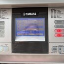Detailní pohled na ovládací panel stříbrného digitálního klavíru. Nad displejem je umístěno logo YAMAHA. Na modrém displeji jsou vidět nápisy TEMPO J…