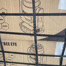 Kartonový obal s černými tiskovými prvky a přetáhnutý černými plastovými pásky. Na krabici je vidět nápis BEE EYE a schéma zařízení s několika hexago…