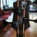 Záhlaví basové kytary z tmavého dřeva s jasnými pruhy. Jsou zde čtyři ladicí mechanismy značky Hypershot a nápis Ce RoHS Compliant. Na zadní straně j…