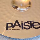 Zlatý kovový činel s povrchem opatřeným jemnými důlky. Uprostřed je umístěno černé logo „pAiste“ a pod ním menší nápis „MADE IN SWITZERLAND“. Povrch…