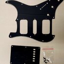 Černý plastový pickguard pro elektrickou kytaru s výřezy pro tři snímače. Vedle něj je umístěn obdélníkový černý kryt s řadou šesti kulatých otvorů.…