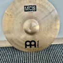 Zlatavý kovový činel s viditelným broušením. Na povrchu jsou nápisy MCS a 20" Medium Ride, v dolní části je logo MEINL. V horní části je malý nečitel…