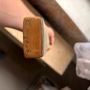 Detailní pohled na hmatník a hran krku strunného nástroje z dřeva světlé hnědé barvy. Na hraně krku je svisle napsaný černý text: 22 NIIUV 1.8. Povrc…