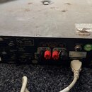 Zadní strana černého rackového zesilovače s kovovým šasi. Na zadním panelu jsou vidět konektory, přepínače a nápisy včetně „SUPPLY AC 220-240V~50Hz“,…
