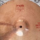 Kovový činel v měděné barvě s viditelným rýhováním povrchu. V horní části je logo Paiste 2002 s nápisy TRADE MARK a MADE IN SWITZERLAND. V pravé část…