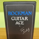 Černý kytarový procesor v plastovém krytu. Na přední straně je modrý nápis ROCKMAN a pod ním bílý text GUITAR ACE by Tom Scholz. Povrch je v dobrém s…