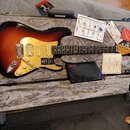 Elektrická kytara typu Stratocaster s barevným přechodem od černé přes červenou k žluté a světlým hmatníkem. Na krytce je nápis „American ULTRA STRAT…