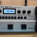 Stříbrný basový efektový procesor s černým výrazným pedálem vpravo. Na horní části je nápis BOSS GT-1B BASS EFFECTS PROCESSOR a na displeji logo BOSS…