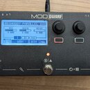 Černý efekt pedál s nápisem MOD DWARF. Uprostřed je displej, na kterém je text SHAGGY PARALLEL BAS a hodnoty MIX 0.680, DRIVE 2.232, DECAY 0.000 a ná…