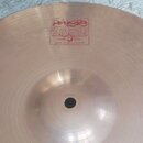 Kružkový činel v bronzové barvě s jemným žilováním povrchu. Na horní části je červený nápis PAIST 2002 TRADE MARK MADE IN SWITZERLAND. V pravé části…