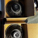 Dvě černé reproduktory v kartonových krabicích. Na horním reproduktoru je v centru logo "JBL". Spodní reproduktor má na rámu nápisy "R 10100 TR 02" a…