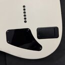 Detail zadní strany bílé kytary. Je zde vidět pět kovových kolíků pro struny, černý plastový kryt elektroniky připevněný šrouby a černý plastový kryt…