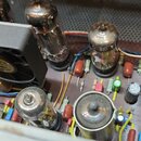 Fotografie zachycuje vnitřek elektronického zařízení, pravděpodobně zesilovače, s několika elektronovými lampami. V horní části je umístěn černý chla…