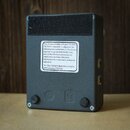 Zadní strana černého, hranatého efektpedálu s matným povrchem. Uprostřed je bílá nálepka s textem: „This device complies with part 15 of the FCC Rule…