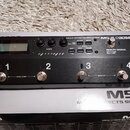 Černý kytarový efektový spínáč Boss MS-3 s kovovým povrchem. Na horní straně je LCD displej, ovládací knoflíky a tlačítka s nápisy LOCK: HOLD > 2 SEC…