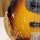 Detail těla basové kytary s barevným přechodem od černé přes oranžovou k žluté. Na levém okrave je vidět rozsáhlé odloupení laku a poškrábaný povrch,…