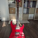 Červená elektrická kytara s výraznou strukturou dřeva na těle. Na hlavě je bílý nápis Washburn a menší označení X. Kytara má dva humbuckery, hриф z t…