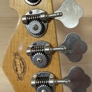 Fotografie zachycuje hlavu basové kytary z přírodního dřeva se čtyřmi stříbrnými ladicími mechanismy. Na dřevě je vidět oválný štít s nápisy „German…
