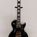 Černá elektrická kytara s gold hardwarem umístěná na černém stojanu. Na hlavě hmatníku je bílý nápis Epiphone. Kytara má dva humbuckery, zlatý most a…
