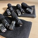 Pět černých mikrofonů s pěnovými čelnicemi a kovovými svorkami. Na svorkách je viditelné logo Audio-Technica. Na těle jednoho z mikrofonů je nápis „A…