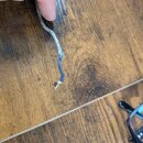 Detailní záběr na konec stříbrného pleteného kabelu. Opletený povrch je v dolní části přetržený a vyčnívá z něj tmavě modré jádro. Kabel leží na hněd…
