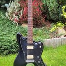 Černá elektrická kytara s tmavým hnedým hmatníkem a světlou hlavou. Na těle je černý pickguard, dva snímače s bílými plastovými krytkami a chromovaný…