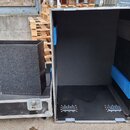 Dvě černé transportní bedny s hliníkovými hranami a kovovými zámky. V levé bedně se nachází šedý, texturovaný hranatý objekt. Vnitřní stěny beden jso…