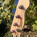 Detail hlavy basové kytary z přírodního dřeva s čtyřmi chromovanými ladičkami. Na dřevě je černý nápis Squier by Fender a PRECISION BASS. Struny jsou…