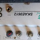 Stříbrný elektronický přístroj s nápisem SKAE0612 a logem SoundKing. Na zadním panelu jsou umístěny různé konektory s popisky OUTPUT, MAIN, MONITOR,…