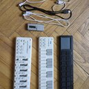 Na fotografii jsou tři bílá a černá MIDI kontrolery značky KORG, tři USB kabely (dva bílé, jeden černý) a stříbrný kovový předmět s nápisem KORG. Prv…