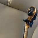 Detail hlavy smyčcového nástroje z dřeva s hnědým lakem a výraznou kresbou zrna. Nástroj má čtyři černé ladičky a zakončení ve tvaru spirály. Na povr…