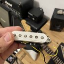 Ruka drží bílý snímač typu single-coil s šesti kovovými póly. Na spodní části je kurzivním písmem nápis Noiseless. Ze snímače vedou žlutý a černý vod…