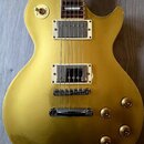 Zlatá elektrická kytara s tmelemi typu humbucker a čtyřmi ovládacími knoflíky. Na přepínači tónů jsou viditelné nápisy RHYTHM a TREBLE. Povrch kytary…