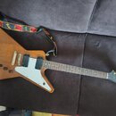 Elektrická kytara s hnědým dřevěným povrchem a bílým pickguardem. Na hlavě hředu je viditelné logo Epiphone. Kytara má dva humbuckery, tři otočné kno…