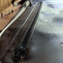 Detailní záběr na hnědý kožený nebo syntetický obal na hudební nástroj. Na fotce je vidět černý zip a část úchytky. Povrch materiálu vykazuje mírné v…