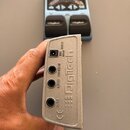 Fotografie zachycuje dva efekt pedály značky Digitech. V popředí je zblízka detail zadní strany stříbrného pedálu s nápisy INPUT, OUTPUT a CONTROL IN…