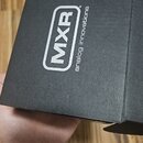 Černá kartonová krabice s matným povrchem. Na boku je bílý nápis „MXR“ v obdélníkovém rámu a vedle něj svislý text „analog innovations“. Krabice vyka…
