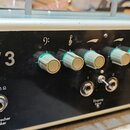 Černý zesilovač v kovovém stříbrném šasi s nápisem MV 3. Na předním panelu se nachází šest šedých otočných knoflíků s nadepsanými symboly basového kl…
