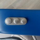 Detail modrého povrchu hudebního nástroje s třemi stříbrnými oválnými ovládacími prvky. Pod prvními dvěma tlačítky jsou viditelné nápisy Effect a Rev…