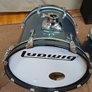 Tmavě modrý basový buben s metalickým povrchem a chromovaným kováním. Na bílém předním koži s nápisem „Ludwig“ je vyřízný otvor. Nástroj vykazuje běž…