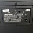 Fotografie zachycuje zadní panel černého elektronického zařízení s různými konektory a nápisy. Jsou zde viditelné vstupy označené jako iPhone / iPod,…