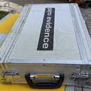 Stříbrný transportní kufr s texturovaným povrchem a hliníkovými hranami. Uprostřed víka je černý svislý pruh s bílým nápisem pro evidence. Kufr má dv…