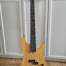 Pětstrunná basová kytara s přírodním dřevěným povrchem těla a hmatníkem z tmavého dřeva. Na hlavě nástroje je svisle napsáno „Marcus Miller Deluxe 5“…
