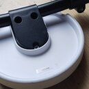 Bílý kulatý stojan s černou kovovou ramenní částí a svěrákem. Na bílé základně je nalepená štítková nálepka s nápisem 19E5446 a pod ní text MADE IN C…